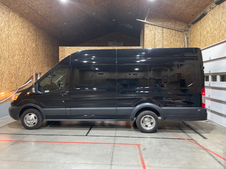 A glossy black rv rental van, likely a converted Ford Transit camper, parked in a warm, wood-paneled garage.