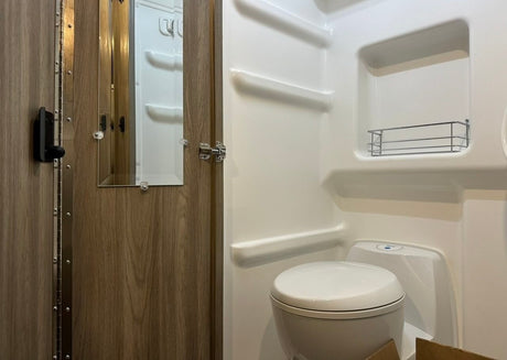 Compact RV rental bathroom with toilet, shower, and mirrored door. Ideal for travel comfort.