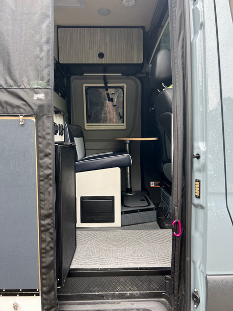 Interior of an RV rental: modern design with a comfortable dinette, window, and storage, seen from the open side door.