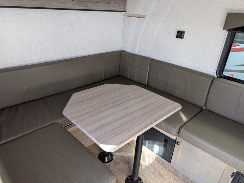 RV rental dinette featuring U-shaped olive-toned cushioned seating, a light wood-grain hexagonal table, and vinyl flooring. — photo 16