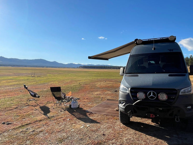 RV rental Sprinter van with awning, chairs, and fire pit in a vast, dry field with distant mountains under a blue sky. — photo 1