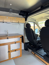 Custom RV rental interior showing a compact kitchenette with wooden cabinets and front seats.