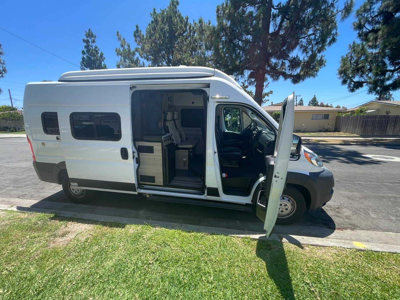  parked curbside on a sunny residential street. Equipped with windows & roof AC.|White camper van with open doors parked on a sunny street — photo 10