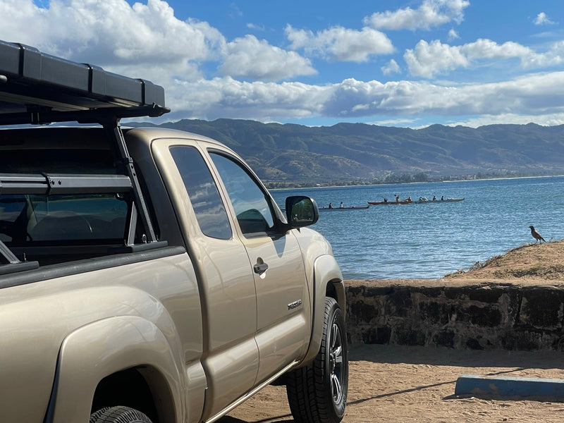 Explore in a tan pickup with a roof-top tent by the ocean. Perfect RV rental for water adventures and mountain views. — photo 1