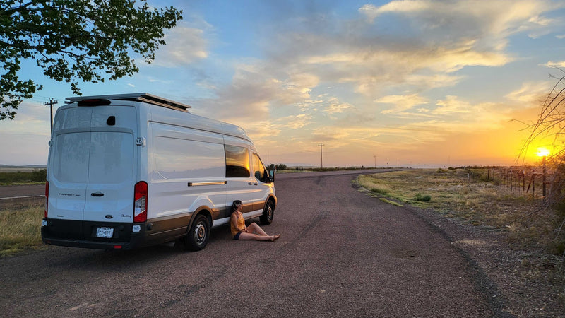 A person relaxes by their white RV rental camper van at sunset, a stunning golden glow over the quiet rural road. — photo 17