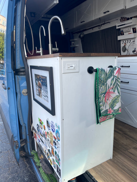 Compact RV rental interior featuring a kitchen with dual sinks, white cabinets, and a tropical towel, perfect for travel.
