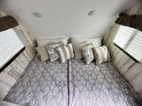 Cozy RV rental bedroom with modern gray & white bedding, multiple pillows, wood-look walls, and bright windows.