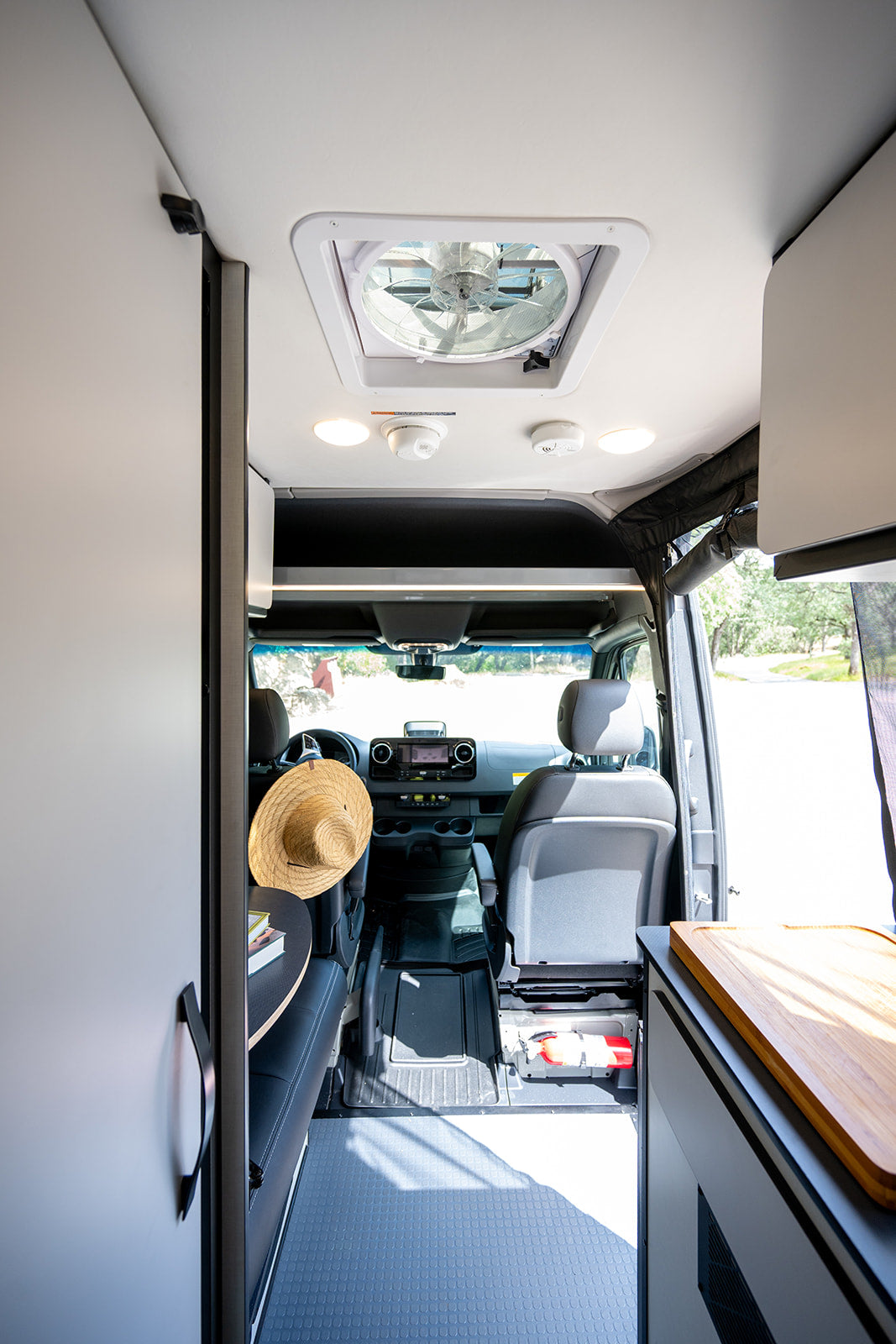 RV rental interior: a sleek, modern van with a ceiling fan, driver's cab view, kitchen counter, and accessible fire extinguisher.