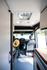 RV rental interior: a sleek, modern van with a ceiling fan, driver's cab view, kitchen counter, and accessible fire extinguisher.