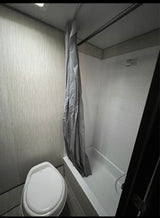 This compact RV rental bathroom features a toilet and a shower/tub combo with a gray curtain.