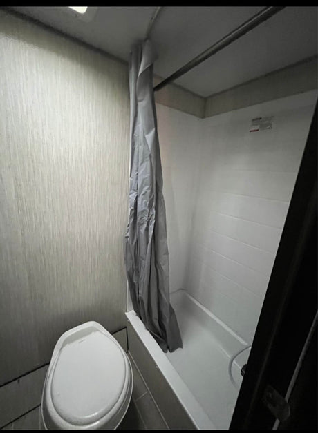 This compact RV rental bathroom features a toilet and a shower/tub combo with a gray curtain.