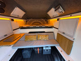 Brightly lit RV rental interior features a bed, sofa, laptop desk, and essential power equipment for comfortable mobile living.