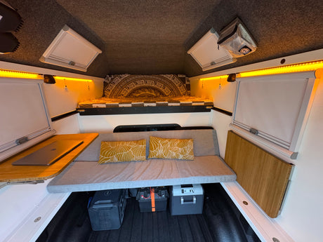 Brightly lit RV rental interior features a bed, sofa, laptop desk, and essential power equipment for comfortable mobile living.
