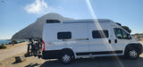 White Winnebago Solis RV rental with bikes by the sunny coast, a mountain in the background. Ready for adventure!