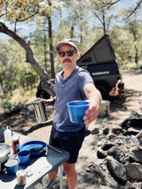 Man offers coffee from his RV rental camp kitchen setup. Ideal for outdoor cooking & adventure trips.