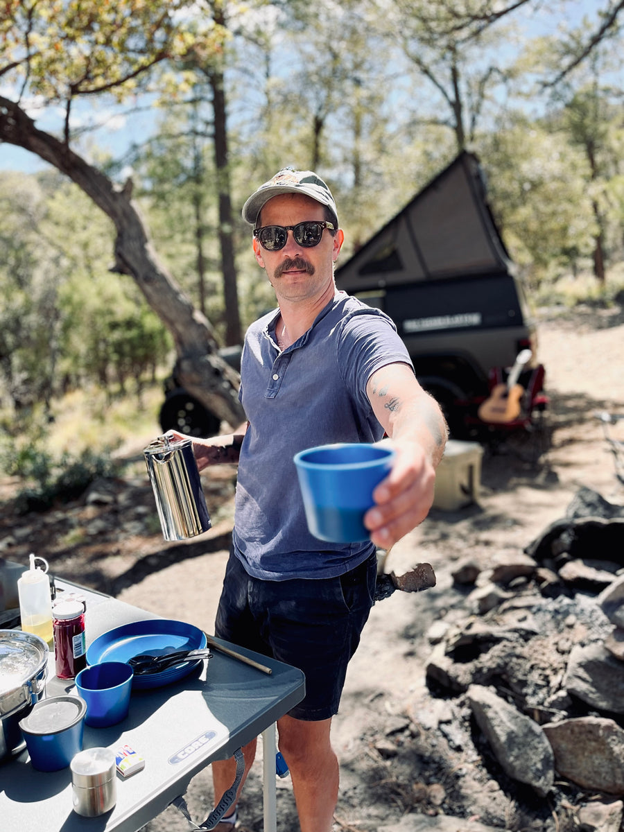 Man offers coffee from his RV rental camp kitchen setup. Ideal for outdoor cooking & adventure trips.