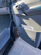 RV rental van: passenger door with handle, storage, speaker, and first aid sticker. Footwell & dashboard visible.