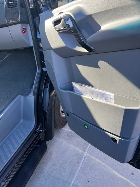 RV rental van: passenger door with handle, storage, speaker, and first aid sticker. Footwell & dashboard visible.