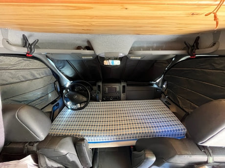 RV rental camper van interior: A front bed occupies the cockpit area, complete with a dashboard and insulated window shades.
