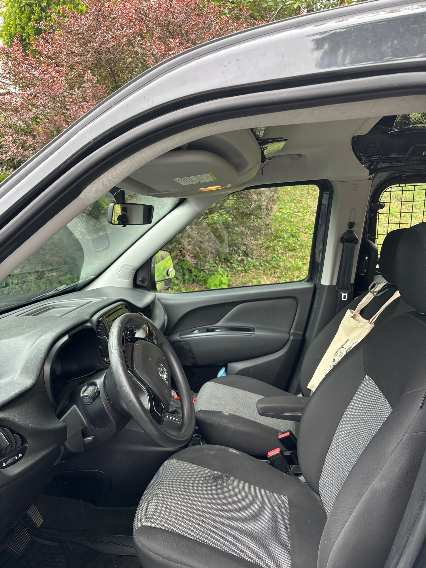 Interior of a compact van's driver cabin, featuring fabric seats and a cargo partition. Ideal for commercial use or a basic RV rental.