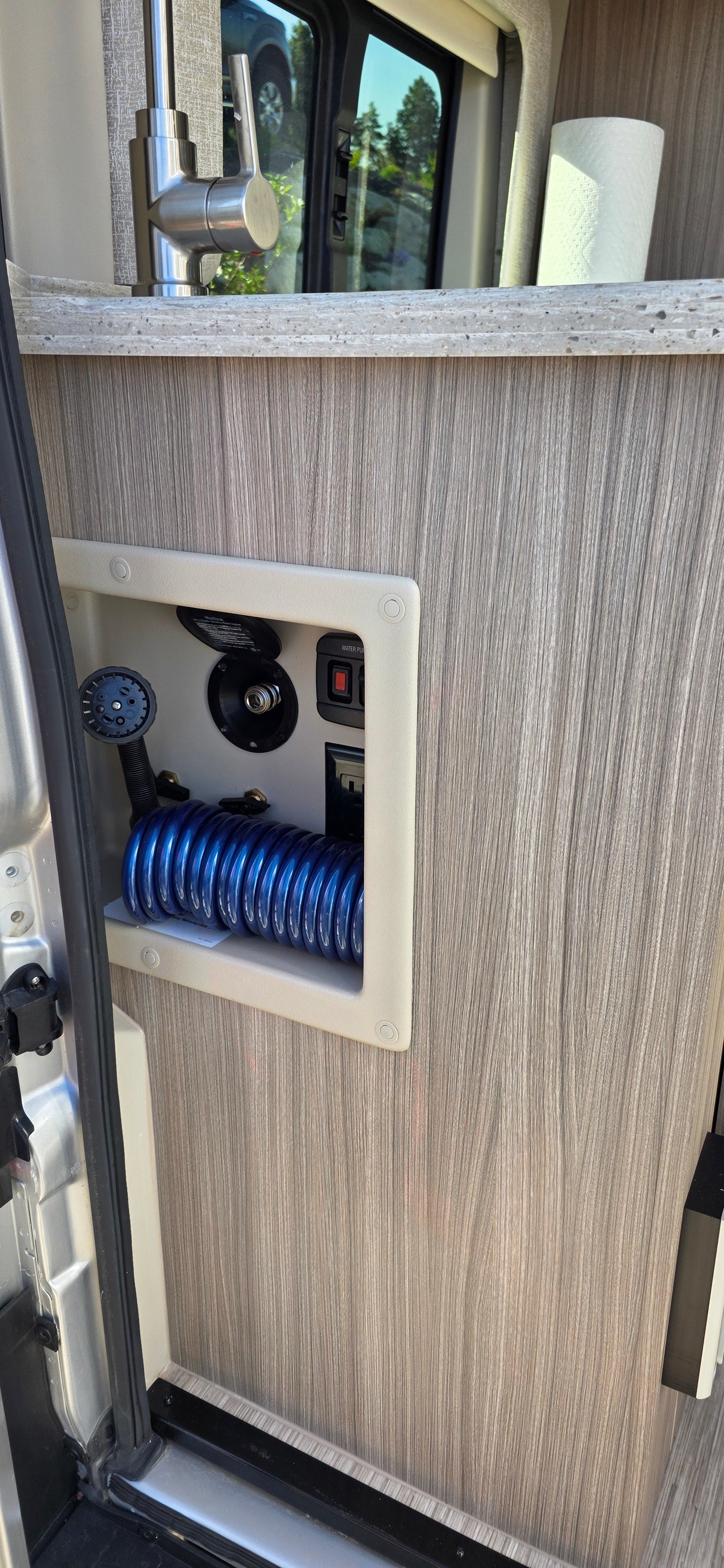 RV rental: Compact kitchen, modern faucet & counter. Lower utility panel offers outdoor shower, water hookup, and pump controls.