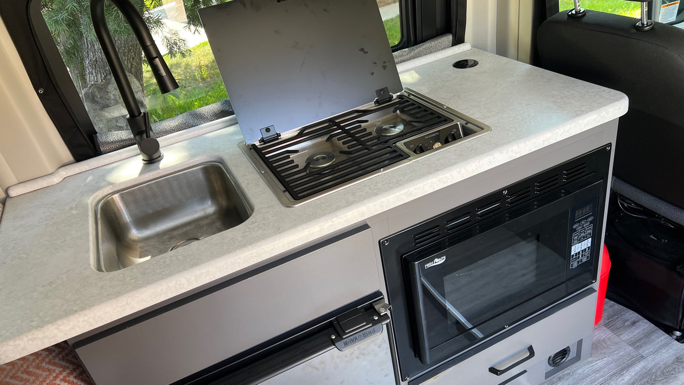 This RV rental's compact kitchen features a stainless steel sink, Dometic stove, High Pointe microwave, and Nova Kool fridge.
