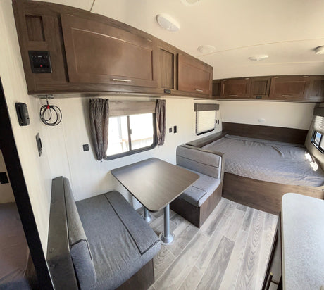 Spacious RV rental interior showcasing a cozy dinette, modern overhead cabinets, and a comfortable bed, perfect for travel.