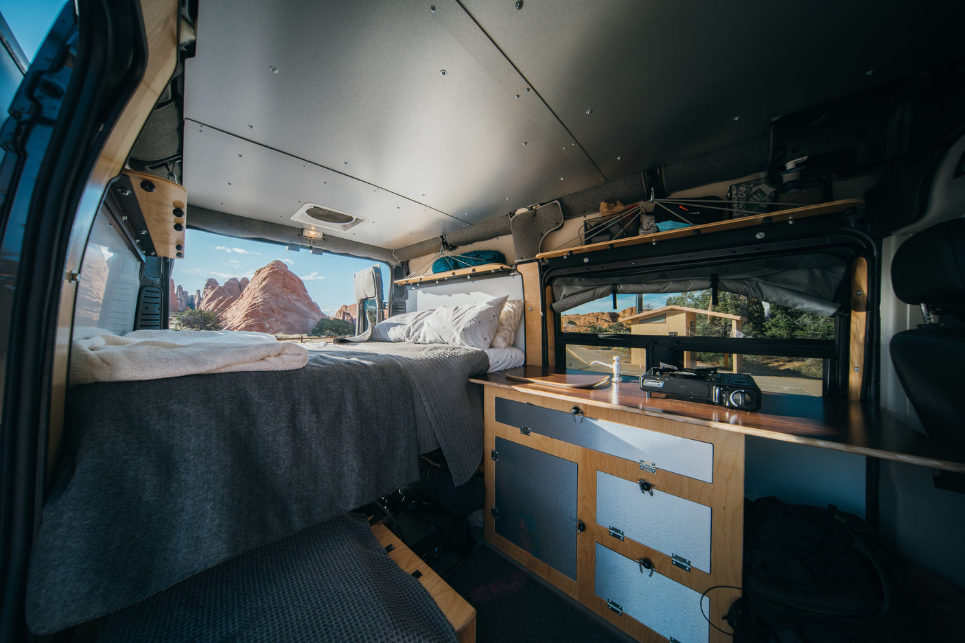 Experience van life in this RV rental. Comfy bed, functional kitchen, & stunning desert scenery outside.
