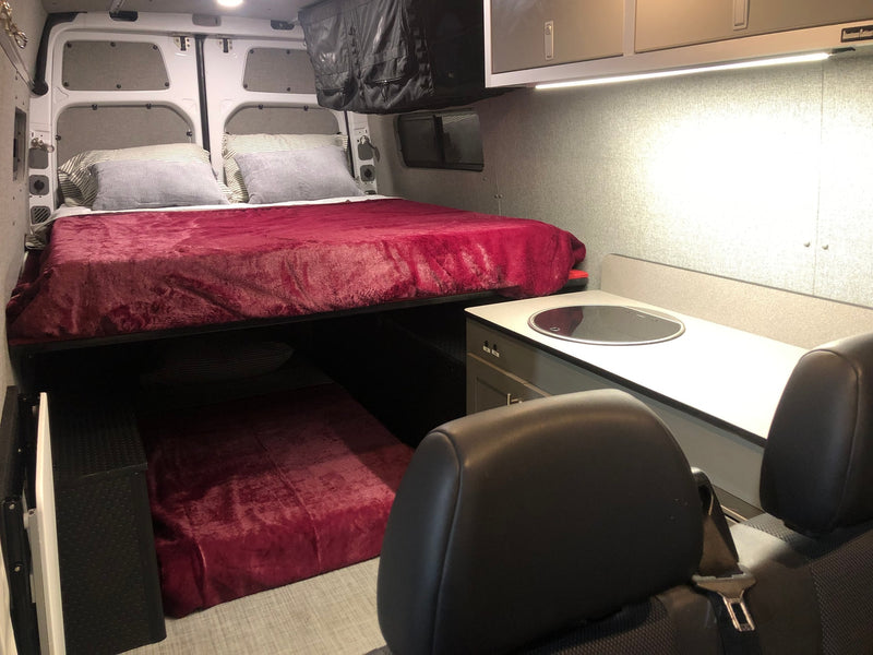 Inside an RV rental: a raised bed with red bedding, a lower bunk, and a compact kitchen counter with sink. — photo 2
