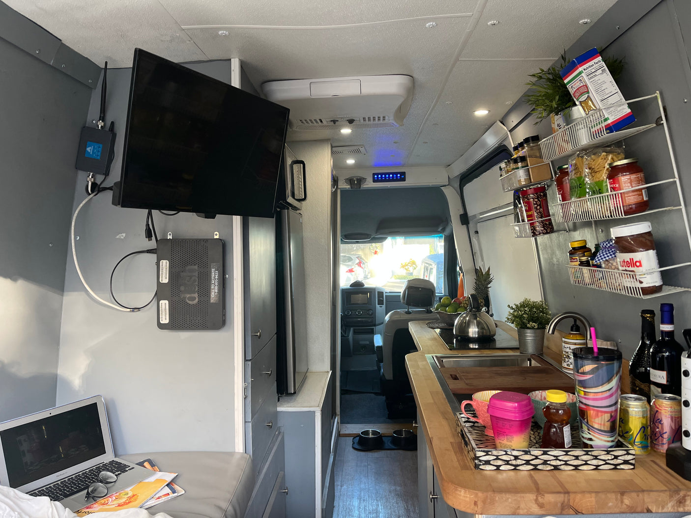 An RV rental interior with a kitchenette, TV, laptop, and pet bowls, perfect for mobile living and travel adventures.
