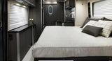 This RV rental features a modern interior with a comfortable bed, compact kitchen, and controls near the window for convenience.