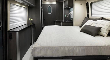 This RV rental features a modern interior with a comfortable bed, compact kitchen, and controls near the window for convenience.