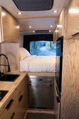 Cozy RV rental interior with bed, kitchen, and wood cabinetry for your next adventure. Enjoy van life with a view!