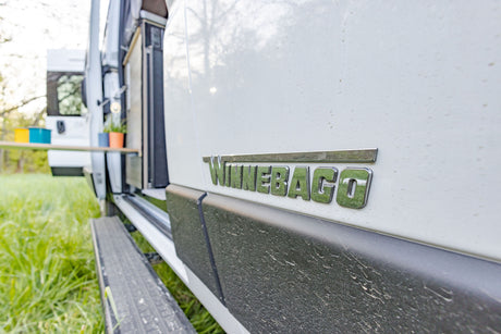 Close-up of a Winnebago RV rental's side panel and logo. This white camper van is ready for an outdoor adventure.