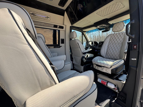 Inside a premium RV rental: comfortable white quilted leather seats, entertainment screens, and a bright, custom interior.