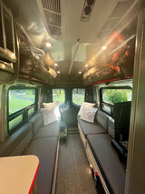 Step into this inviting rv rental, showcasing parallel bench seating, plush pillows, overhead storage, and scenic windows.