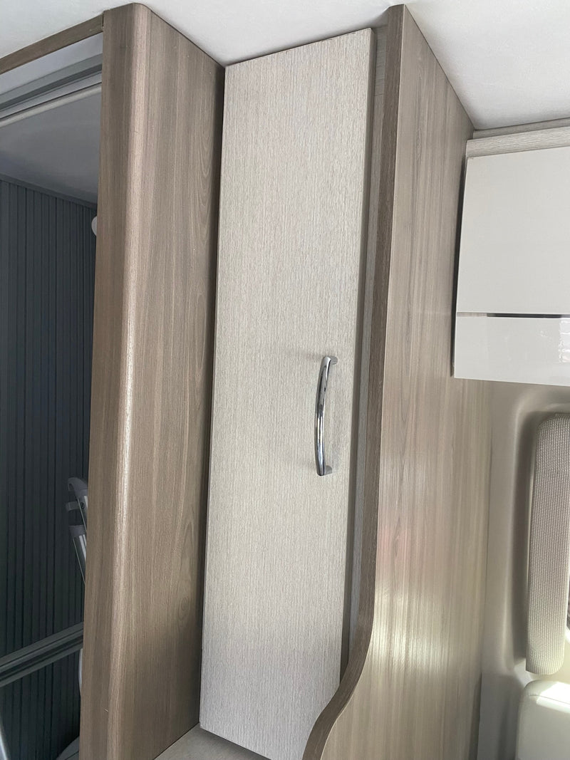 RV rental interior: close-up of light wood-grain walls, a textured cabinet door with a silver handle, and overhead storage. — photo 10