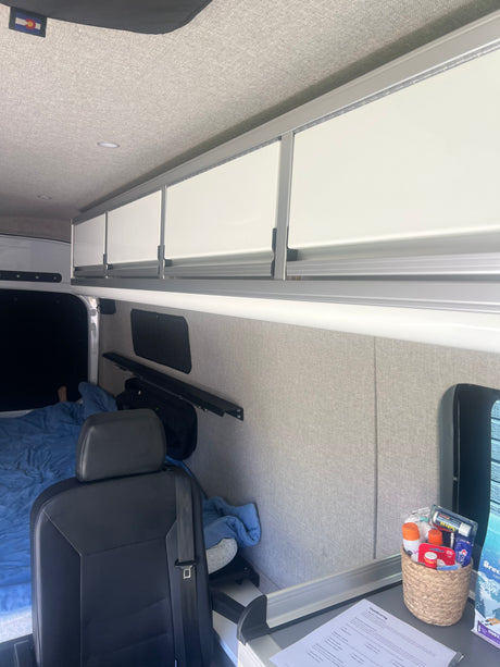 Inside a cozy RV rental: fabric walls, overhead cabinets, bed, and "Outdoorsy" checklist for your next adventure.