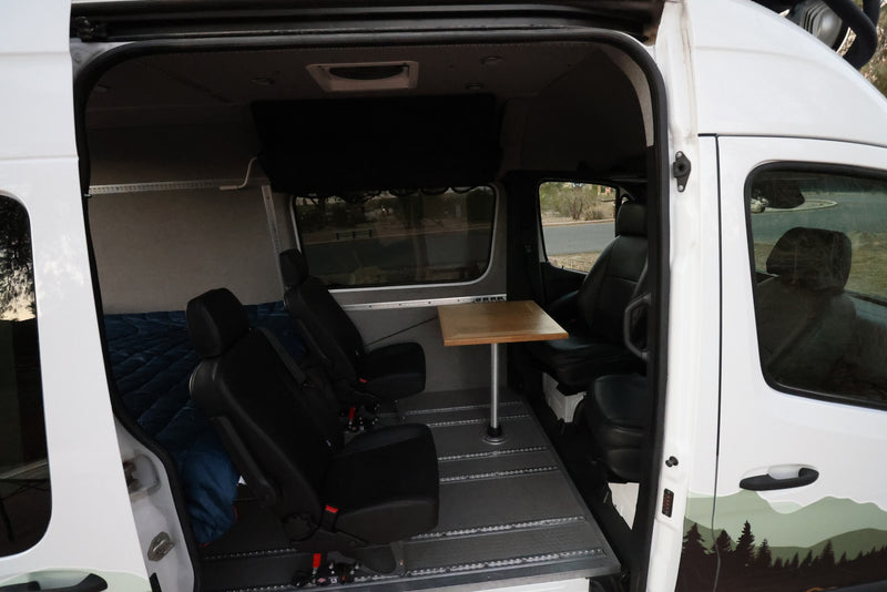 View inside a white RV rental: black modular seating, wood dining table, and a bed in the rear. — photo 16