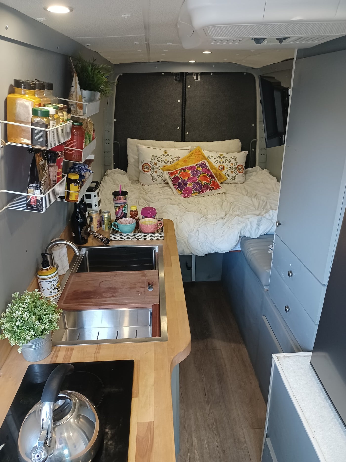 Experience comfort in this rv rental. The interior features a cozy bed with colorful pillows and a well-equipped compact kitchen. — photo 7