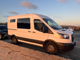 White Ford Transit RV rental parked at sunset. This camper van has a flat front tire, temporarily pausing its road trip.