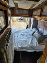Cozy camper van interior, perfect for an rv rental, featuring a comfortable bed, overhead cabinets, and open rear doors to the outside.