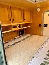 Cozy RV rental interior featuring a comfortable bed with a cable-knit blanket, wooden cabinets, and storage.