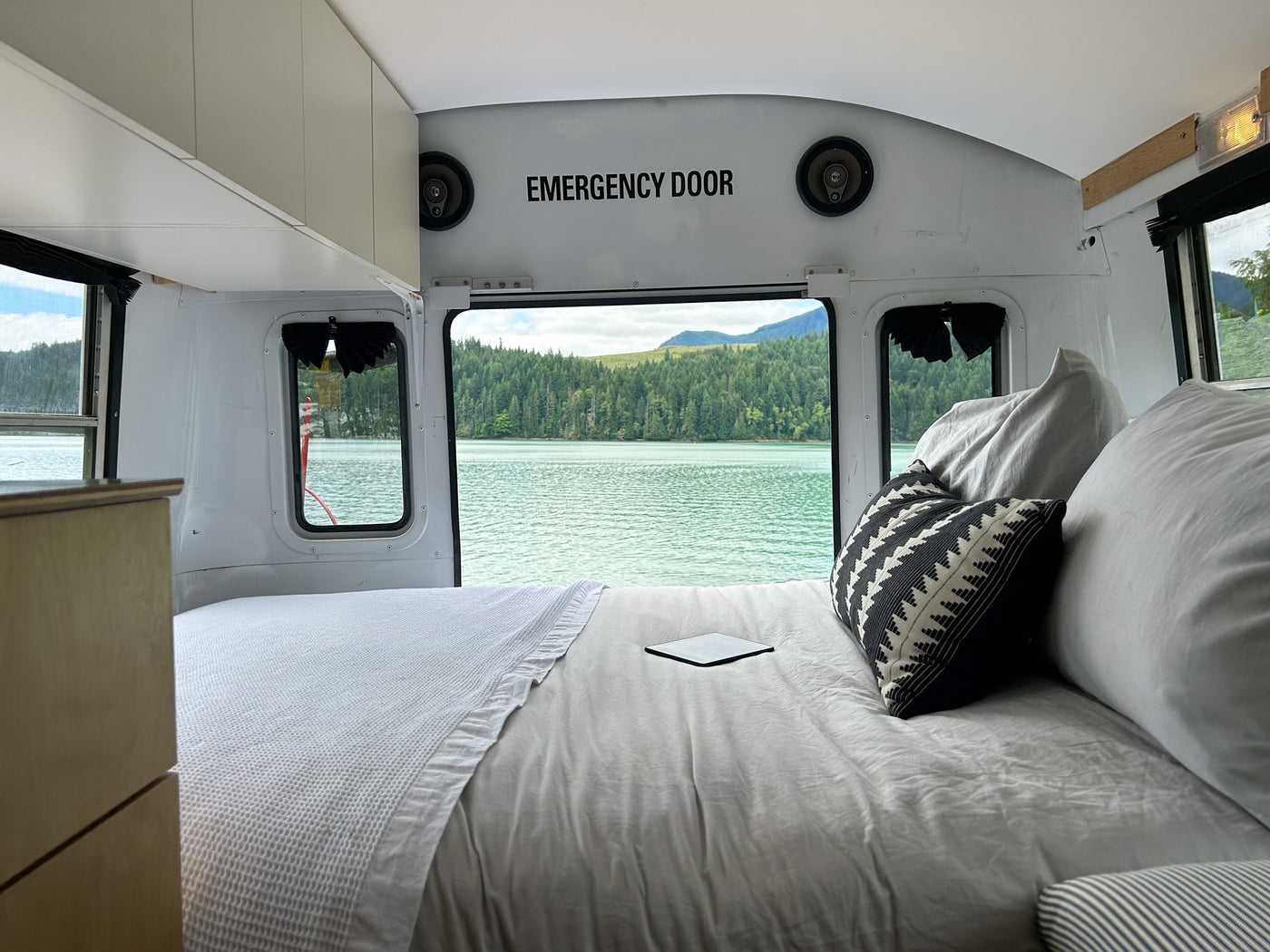 Cozy RV rental bedroom with a breathtaking water view from the rear emergency exit. Features a large bed and cabinets. — photo 5