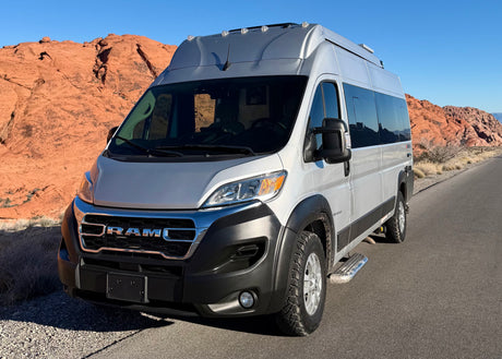 Silver Ram RV rental on a desert road with red rock mountains under a blue sky, ready for adventure and scenic travel.