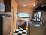 Inside an RV rental: a cozy space with a checkered floor, kitchenette, and dining nook, perfect for road trips.