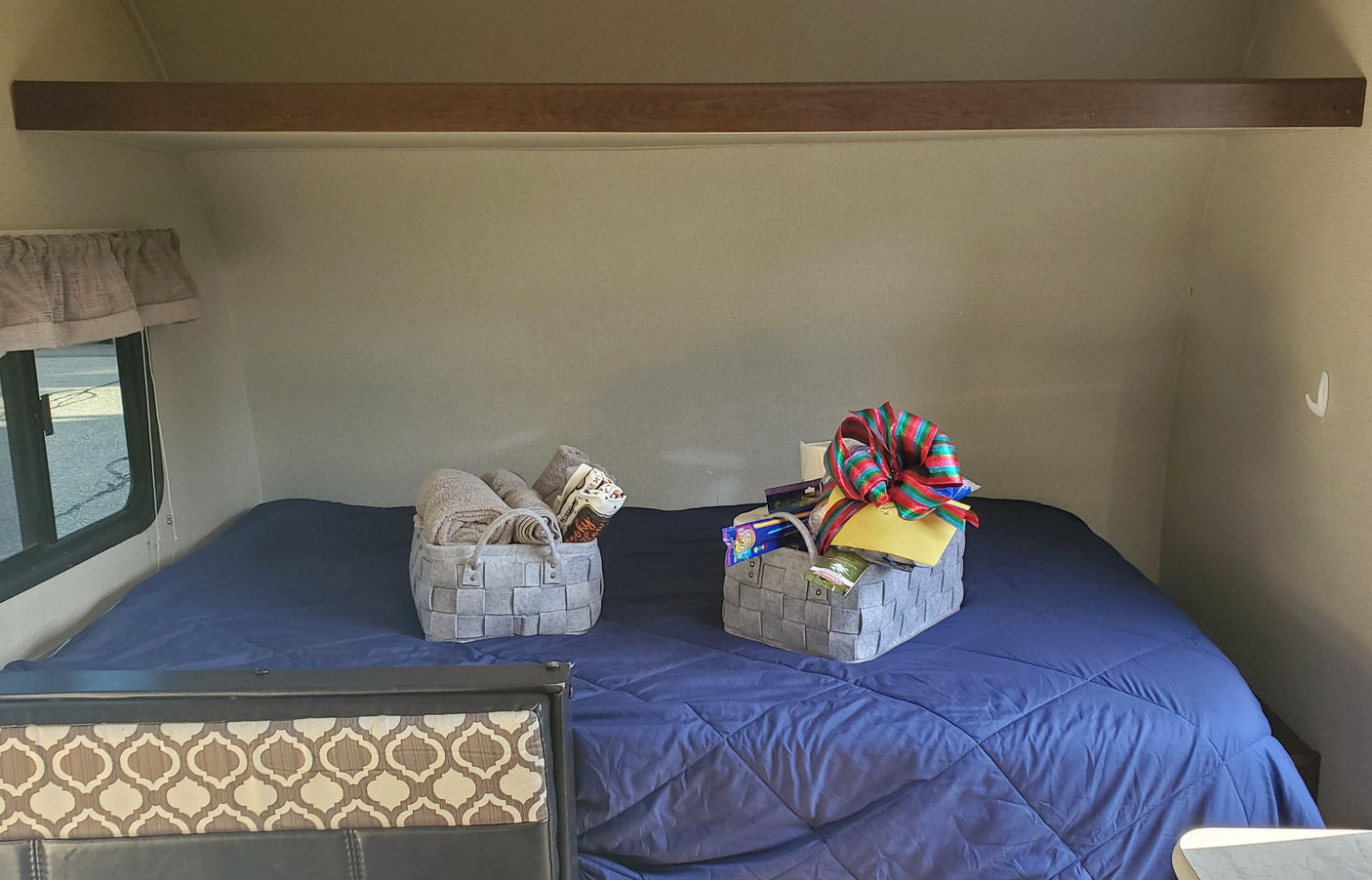 Cozy RV rental bedroom with a blue bed and welcome baskets, including towels and a gift. Ready for your comfortable journey.