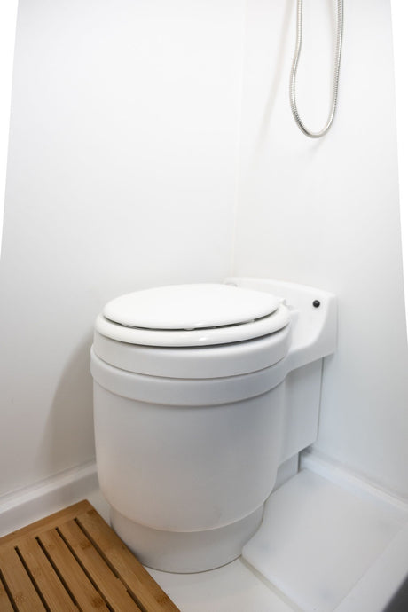White toilet and silver shower hose in an RV rental bathroom, with a wooden floor mat.