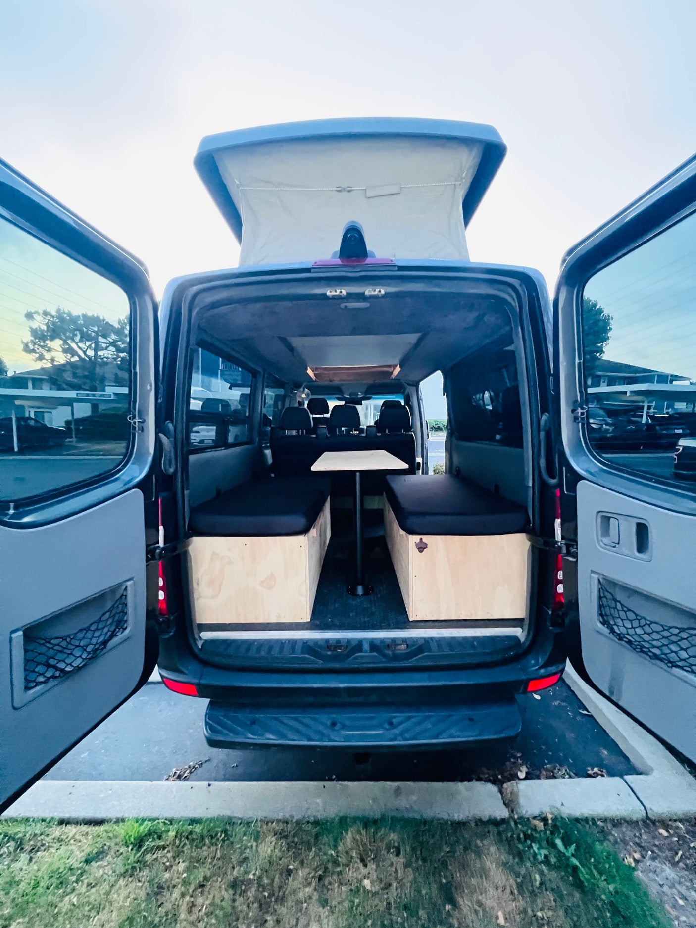 This RV rental showcases a pop-top camper van's customized interior with benches, cushions, and a table, ideal for travel.