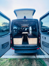 This RV rental showcases a pop-top camper van's customized interior with benches, cushions, and a table, ideal for travel.